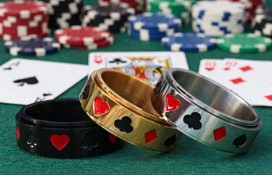 POKEROO Spinner Ring in black, gold, and silver stainless steel bands with card suit symbols, shown with poker chips and playing cards